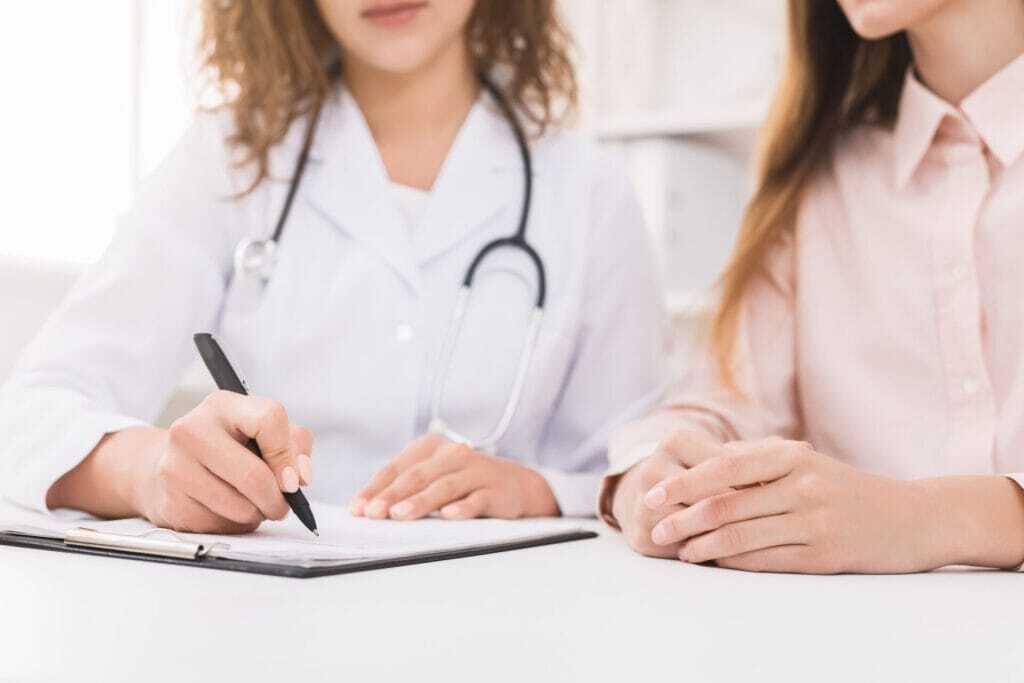 A doctor writing notes on a clipboard while sitting with a patient during a consultation.