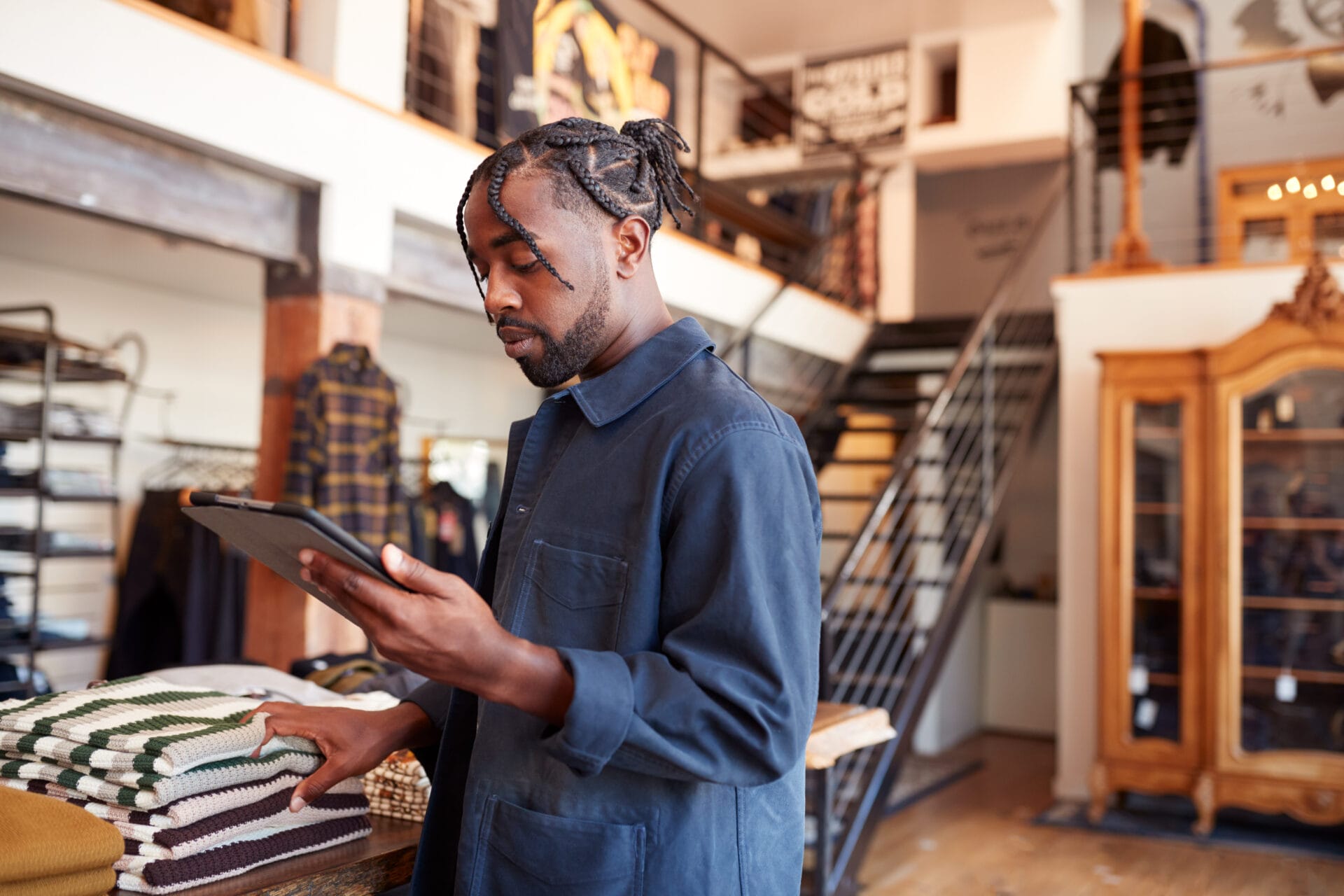 Retail worker organizing folded clothes while using a tablet, showcasing the role of on-demand hiring for seasonal efficiency.